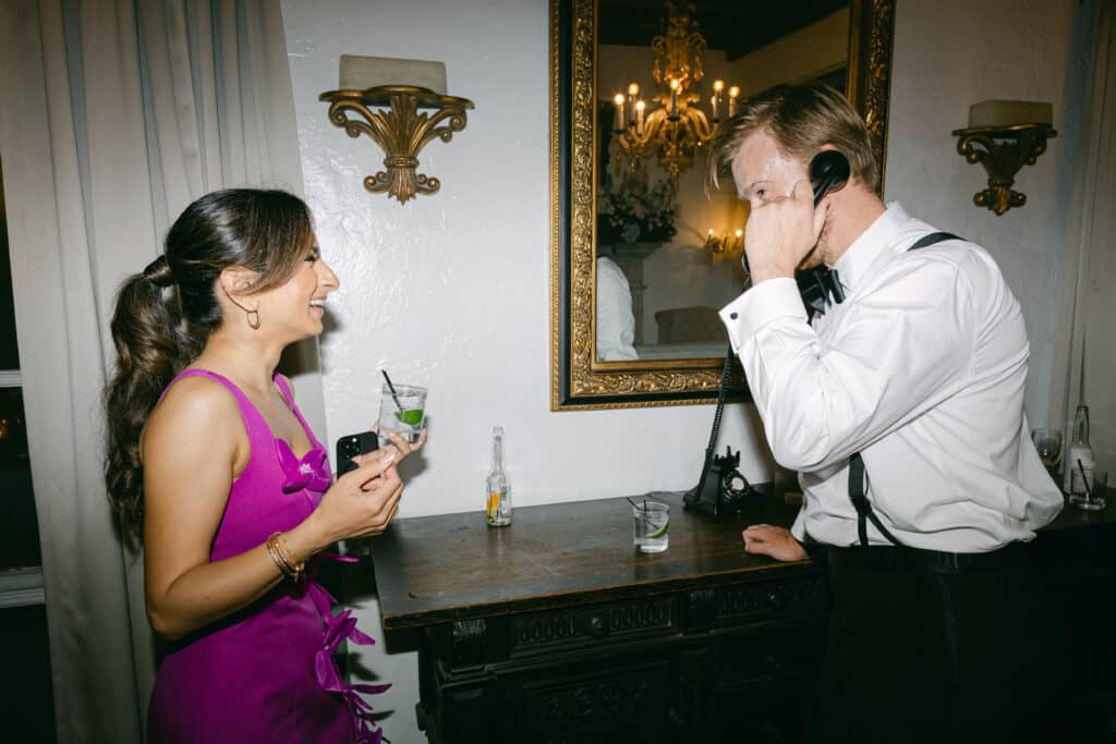 Man and woman laughing while using a phone at a wedding